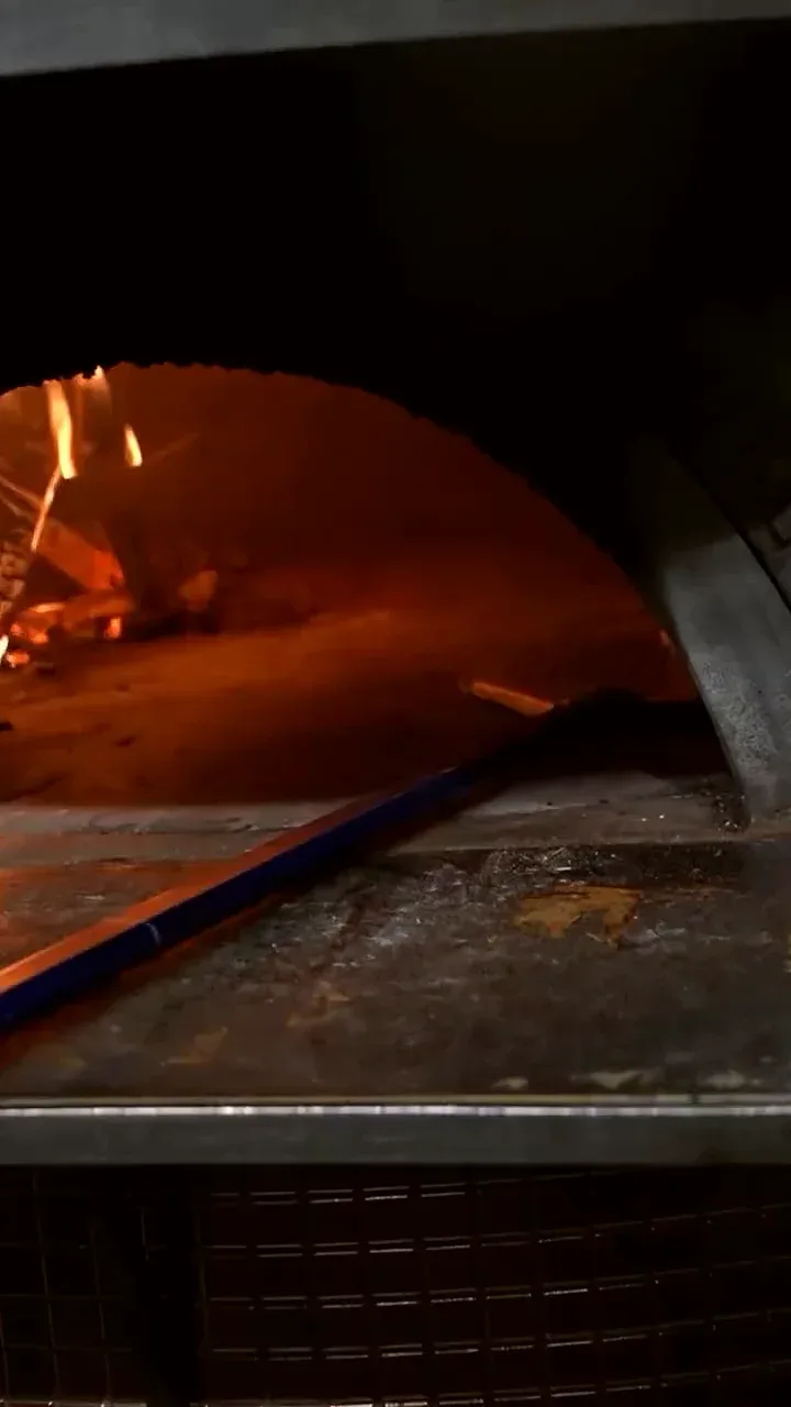 Pizza enfournée à la pelle dans le four à bois en mosaïque cuivrée, flammes vives
